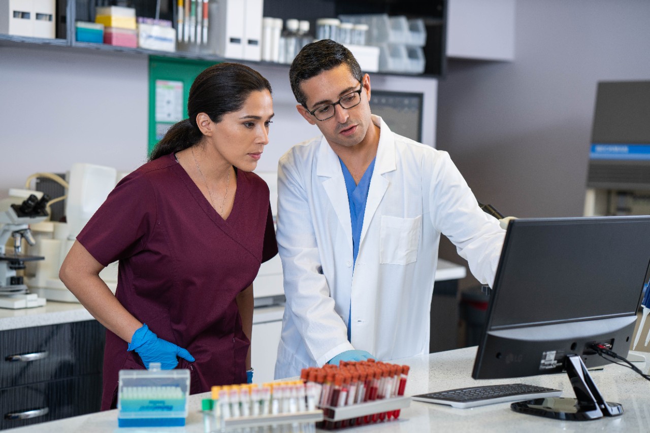 Laboratory technician and assistant looking at computer monitor