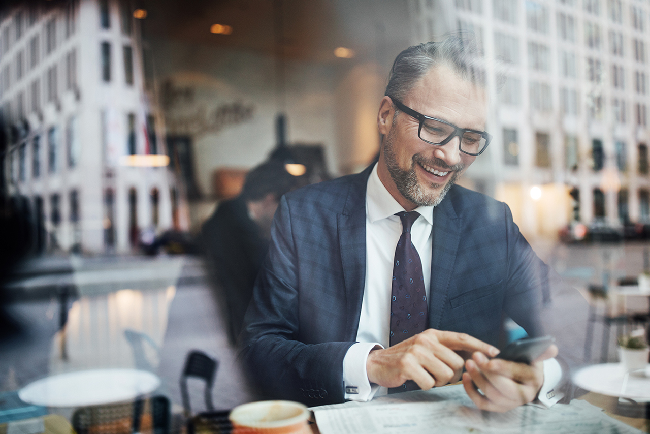 Mature businessman sitting inside at cafe and using mobile phone. Mid adult male texting with his smart phone at coffee shop.