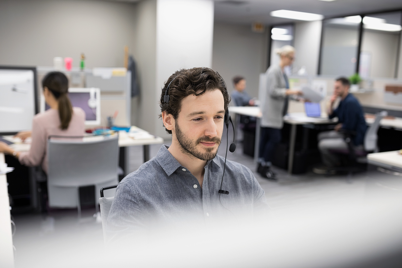 Man smiling in office with headset looking at computer