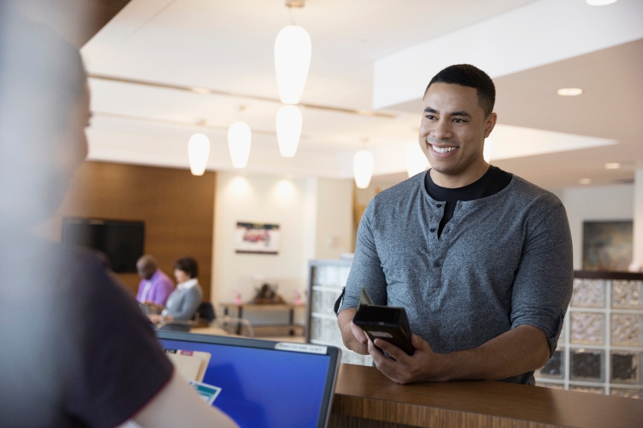 Smiling male patient paying insurance copayment with credit card reader at clinic check-in counter