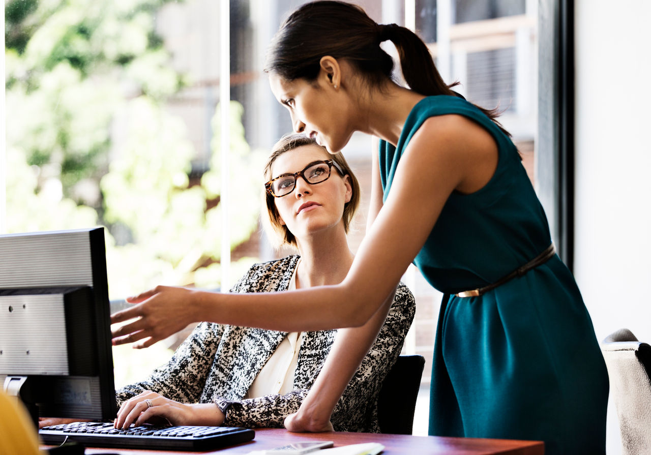 Businesswoman explaining something to female colleague over computer at desk in office