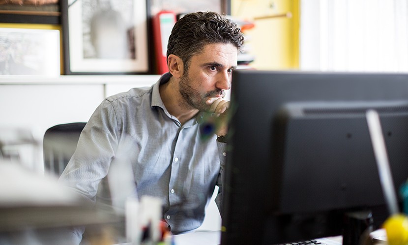 Mature man sitting at his desk and looking at camera with serious expression at textile shop. Textile shop owner working at his desk.